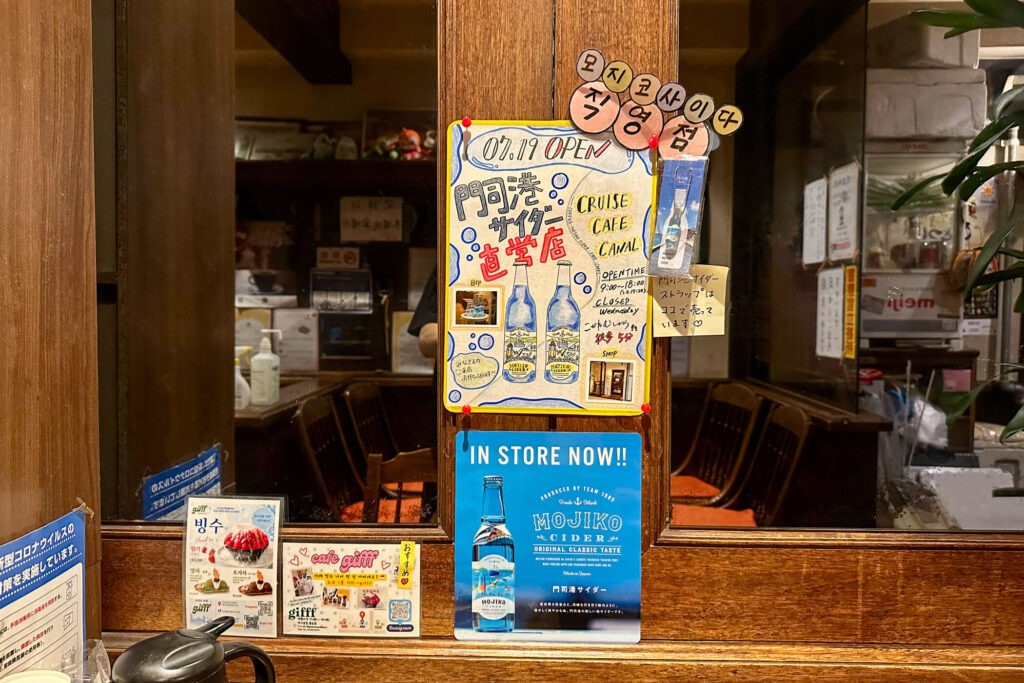 こがねむし店内に掲示された門司港サイダーと直営店Cruise Cafe Canalの案内